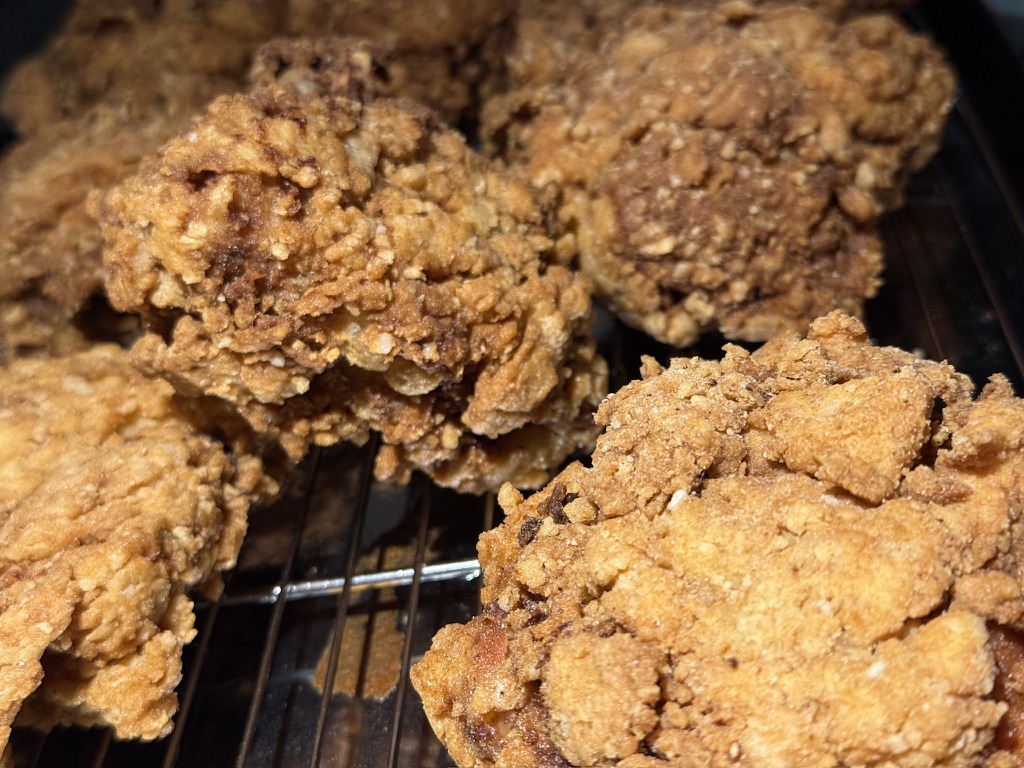 Close-up of golden fried chicken pieces with a craggy, textured crust resting on a wire rack