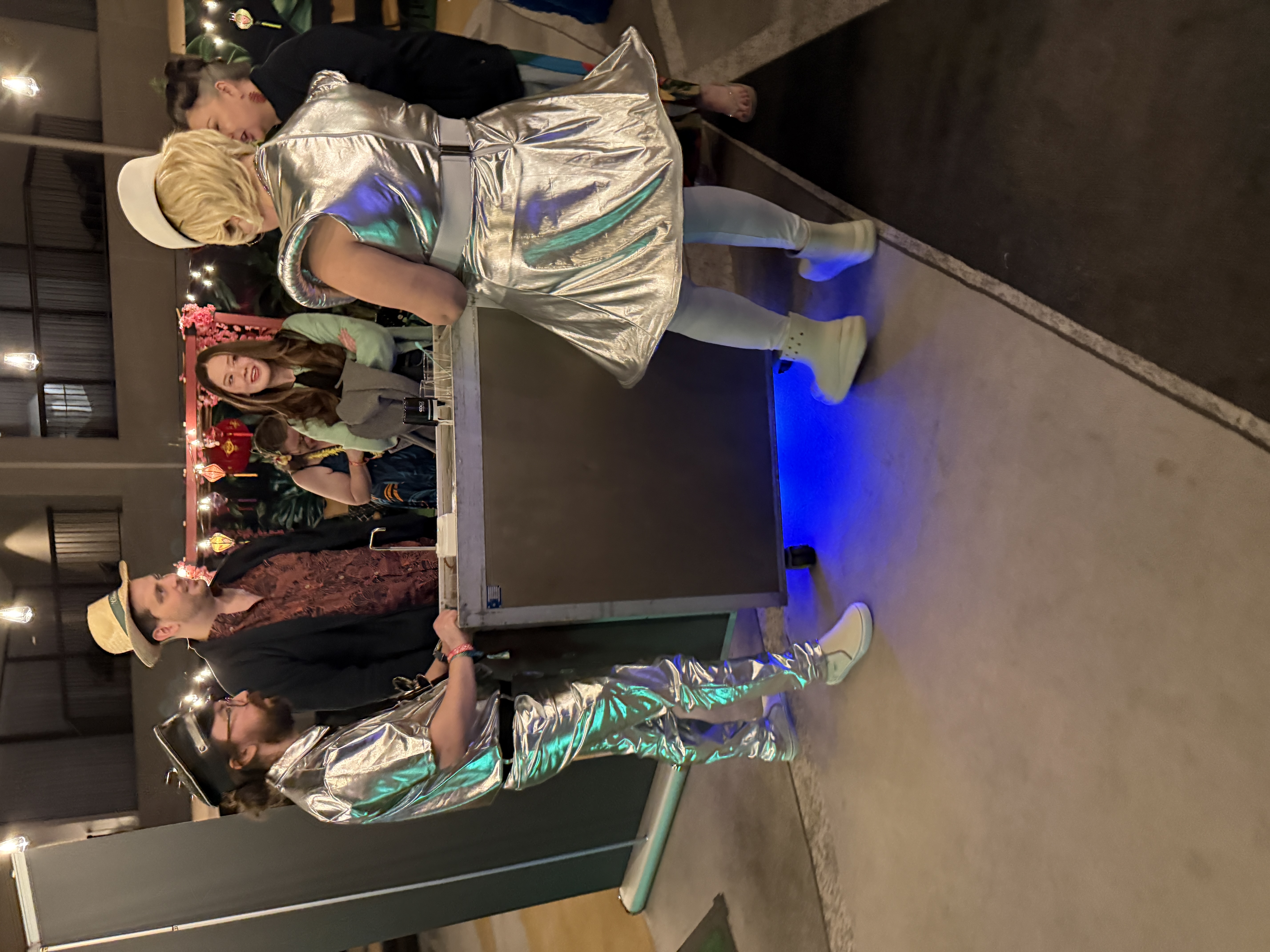 Two people in matching silver space suits at a mobile bar cart