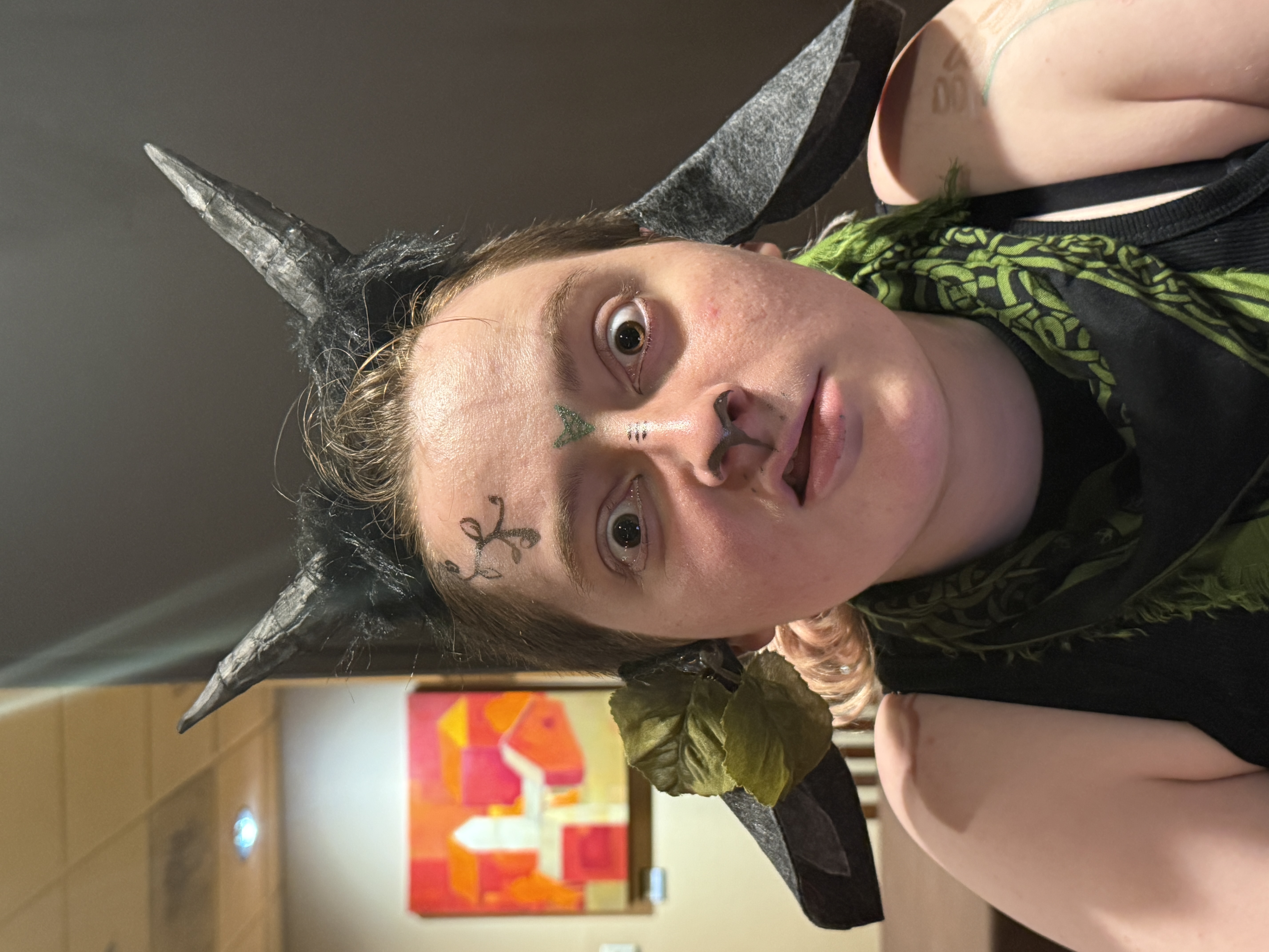 Juniper's improvised cottagepunk goat, horns and ears made from scratch in the hotel room. A young person in an improvised cottagepunk goat costume with handmade black horns, pointed ears, green face paint markings, and leafy accessories