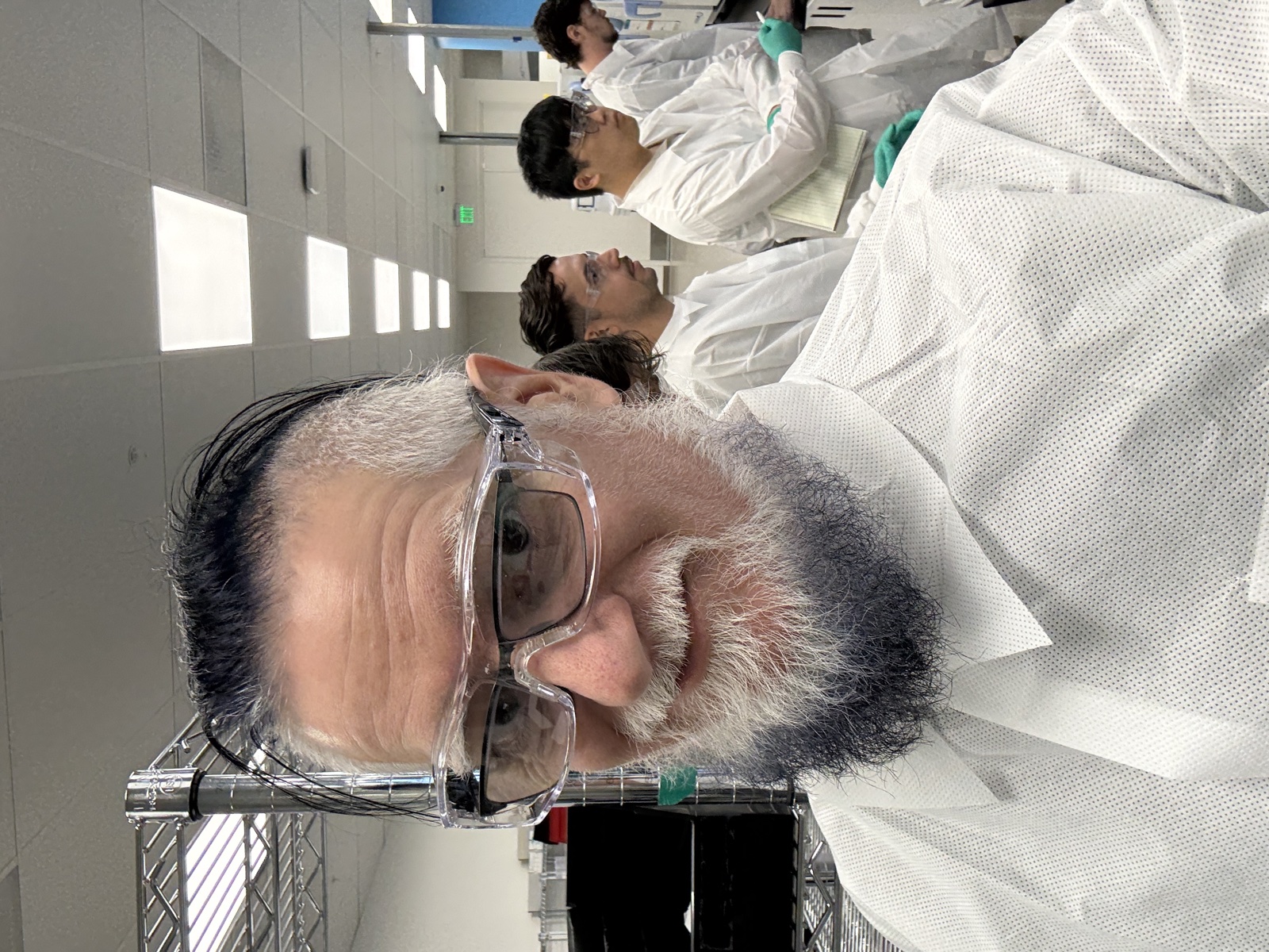 Eric in the Natera histology lab wearing safety goggles and a white lab coat, with scientists working at stations behind him