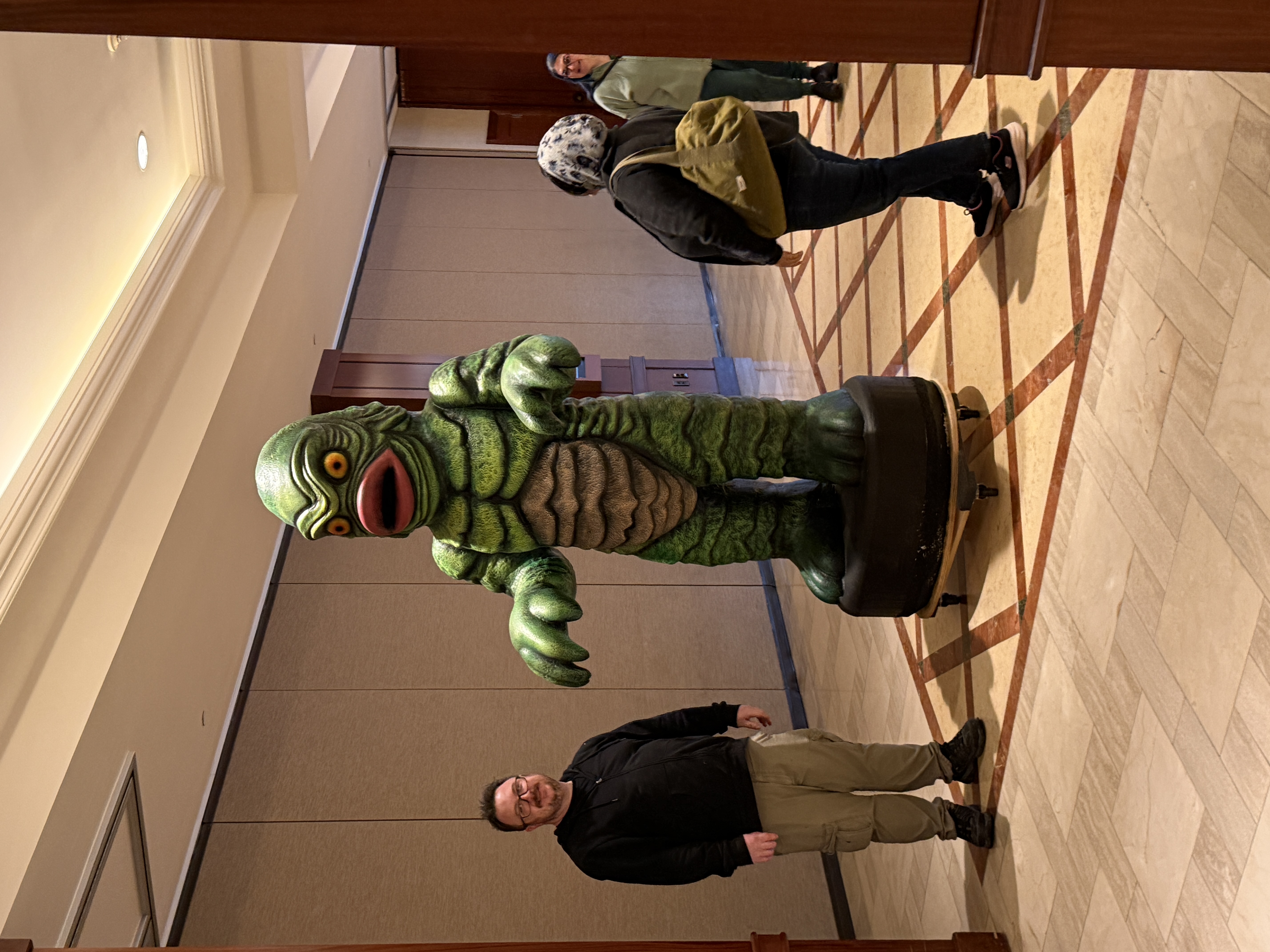 Person standing next to a large Creature from the Black Lagoon statue in a hotel hallway