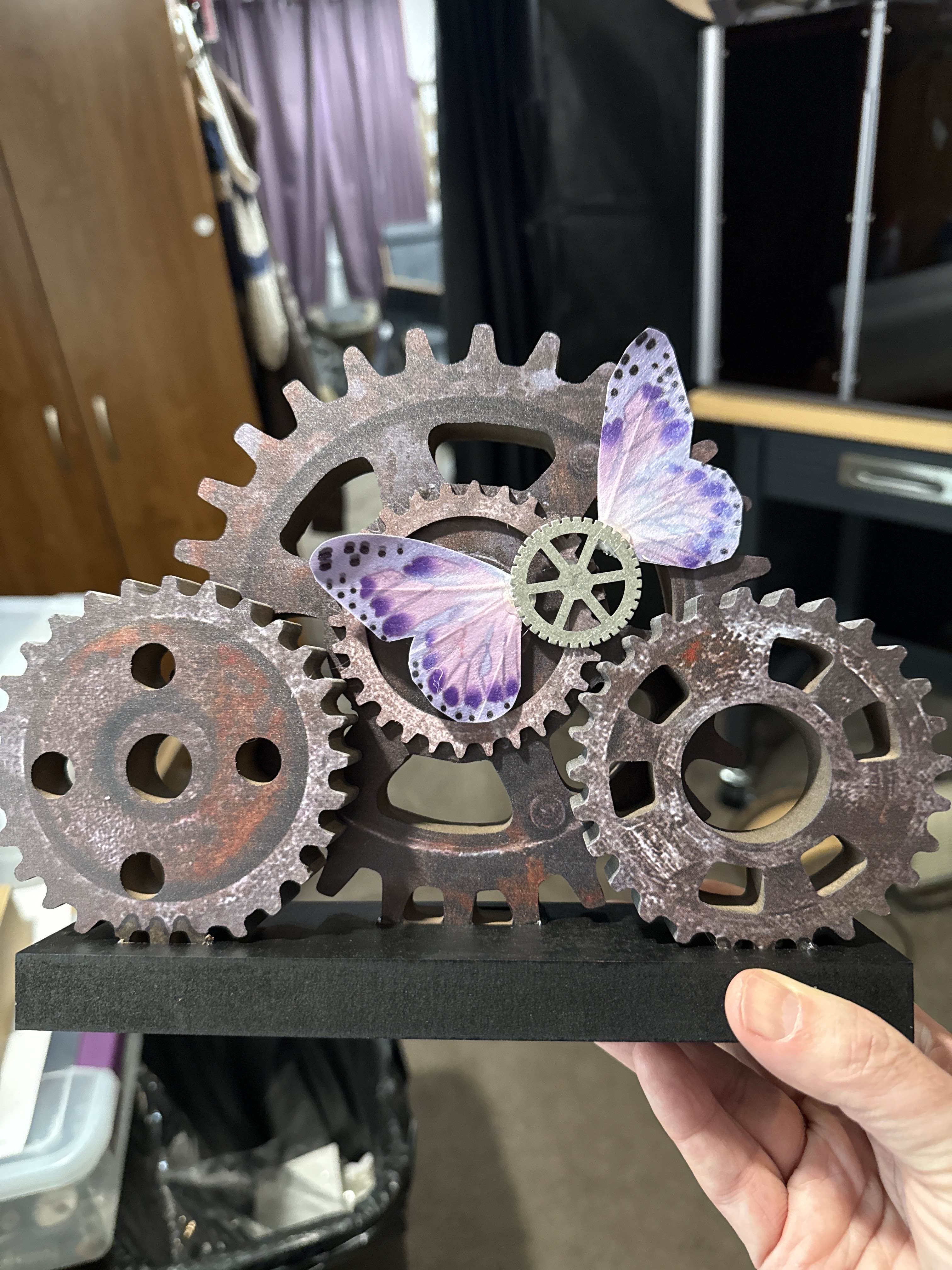 One of three costume contest trophies. The base was purchased and I added the winged gear from bits and bobs. A costume contest trophy made of interlocking steampunk gears with a purple butterfly perched among them, mounted on a black base