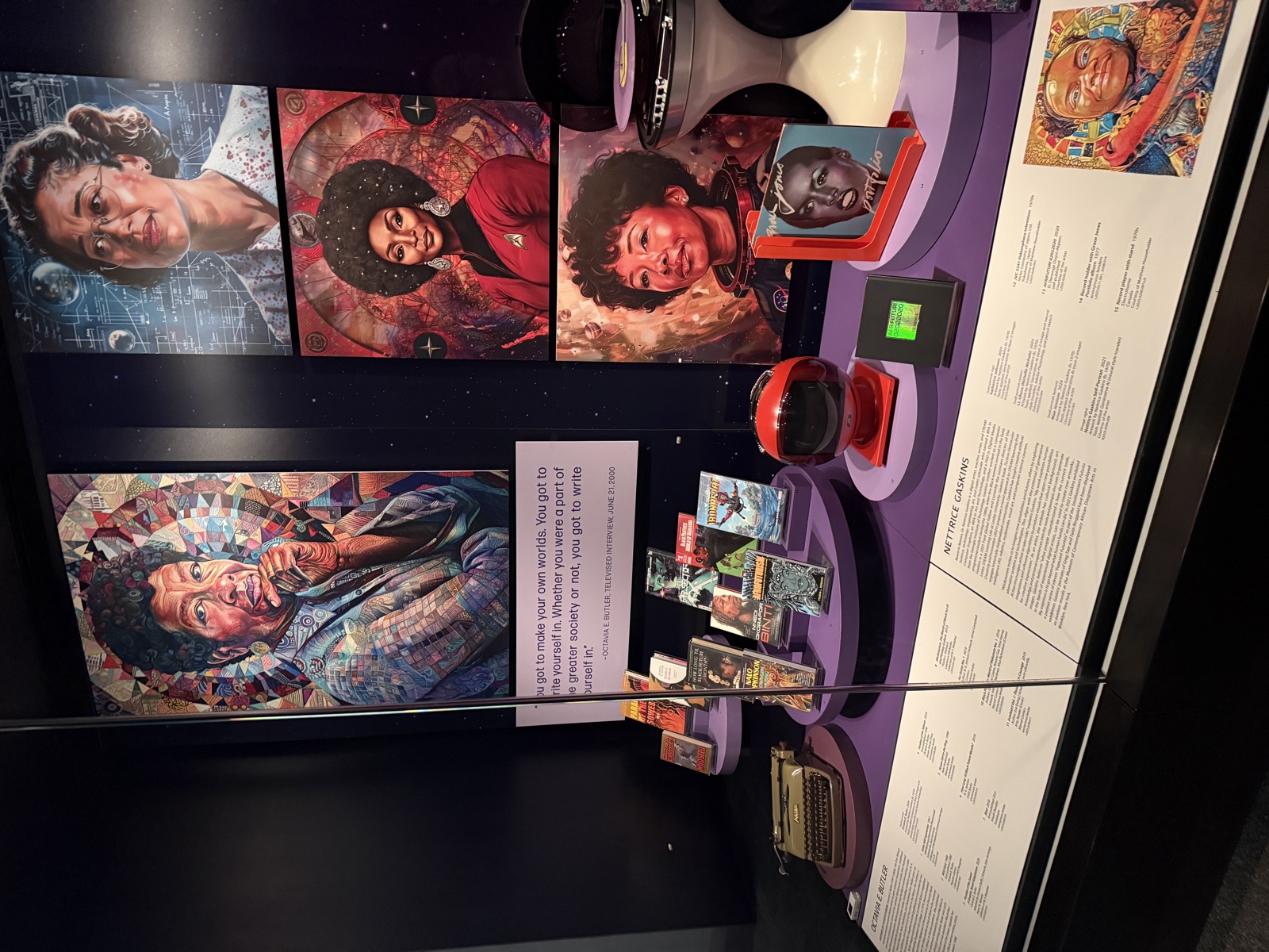 The Octavia Butler section of the Women of Afrofuturism exhibit at SFO, featuring her typewriter, books, and portraits by Nettrice Gaskins alongside depictions of Nichelle Nichols and other figures