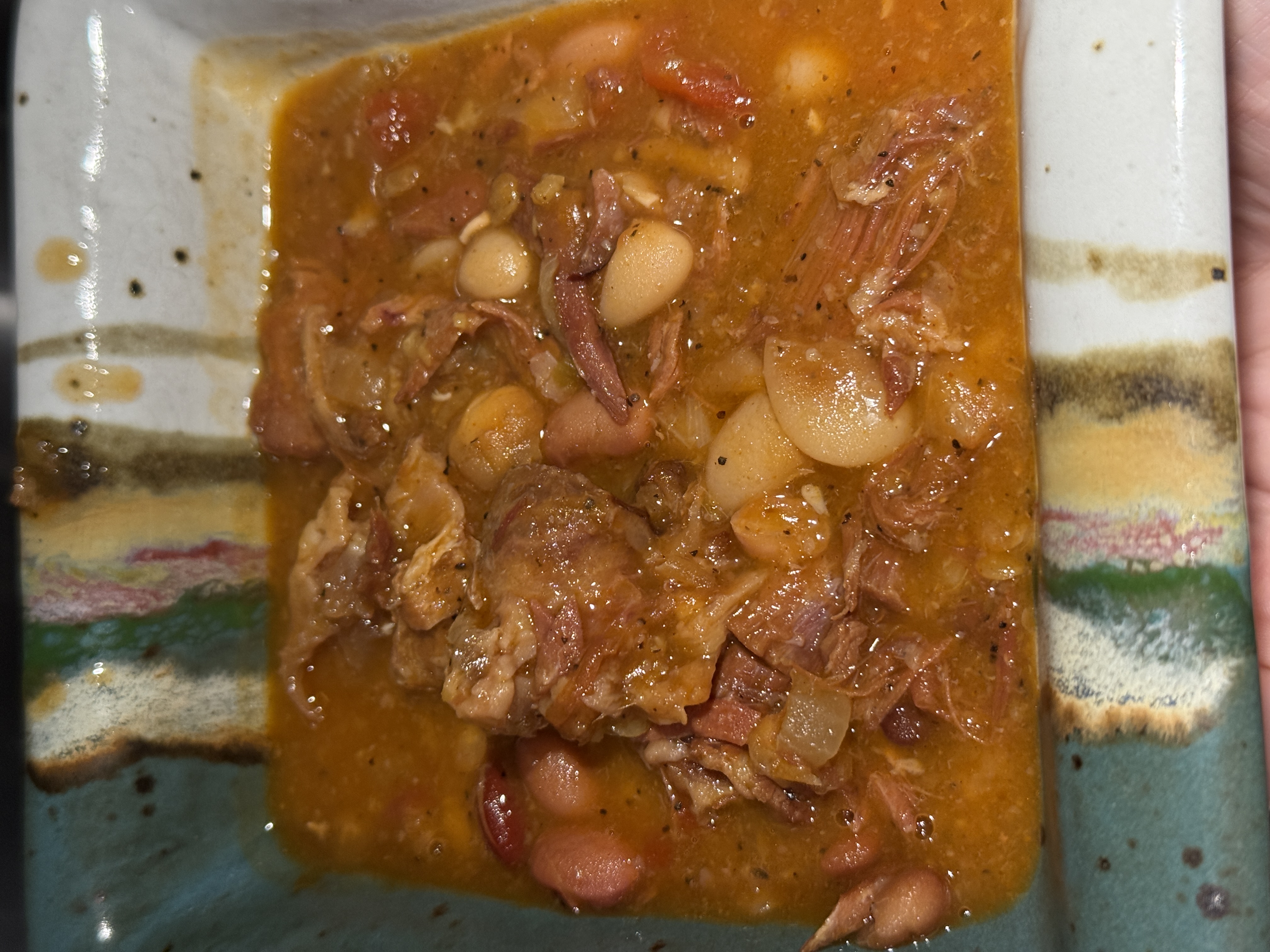 A bowl of fifteen-bean soup with shredded ham in a handmade ceramic bowl with blue and green glaze